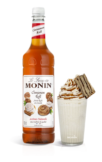 A bottle of Monin Cinnamon Roll Syrup with a glass of syrup-enhanced beverage and a cinnamon roll pastry.