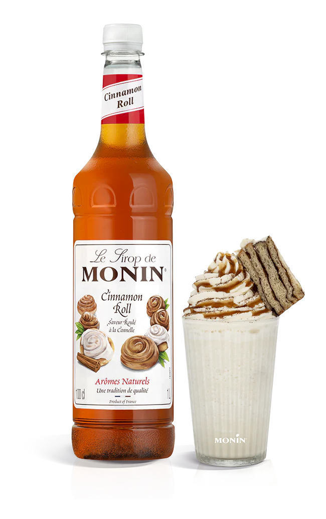 A bottle of Monin Cinnamon Roll Syrup with a glass of syrup-enhanced beverage and a cinnamon roll pastry.