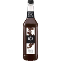 Promotional display featuring 1883 Dubai chocolate syrup bottle alongside iced drink and pistachio chocolate bars against Dubai skyline