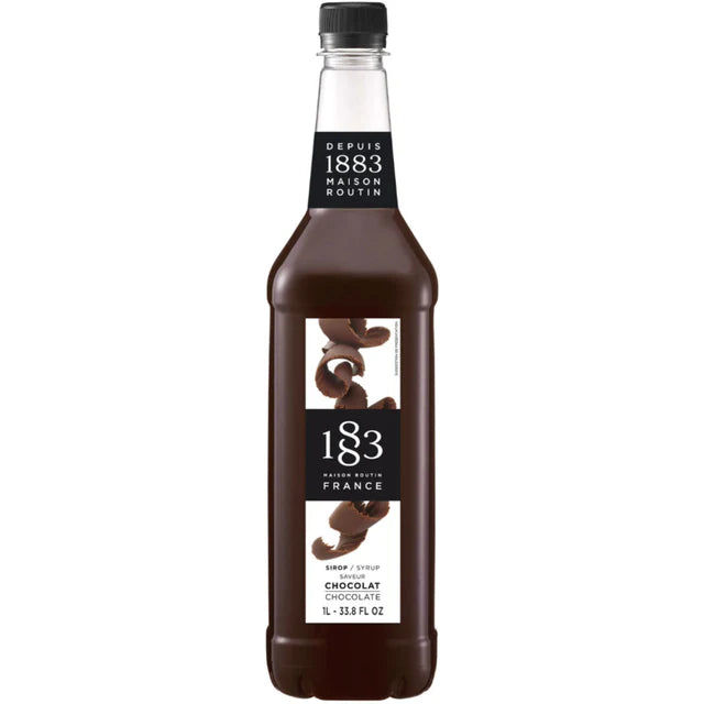 Promotional display featuring 1883 Dubai chocolate syrup bottle alongside iced drink and pistachio chocolate bars against Dubai skyline