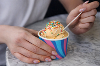 Lifestyle photograph showing hands holding patterned 8oz ice cream tub filled with orange ice cream and rainbow sprinkles.