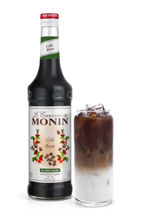 A bottle of Monin Cold Brew Concentrate next to a glass filled with ice and a serving of the concentrate, showcasing a creamy brown liquid.