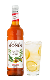 Monin Hot Honey syrup bottle with a glass of lemonade on a white background