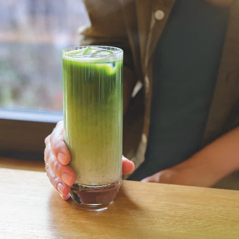 Matcha pistachio mango mocktail in tall glass with monin syrup layered green drink held by hand