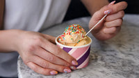 Realistic stock photograph depicting hands holding medium patterned ice cream tub (6oz) filled with ice cream and colorful sprinkles.