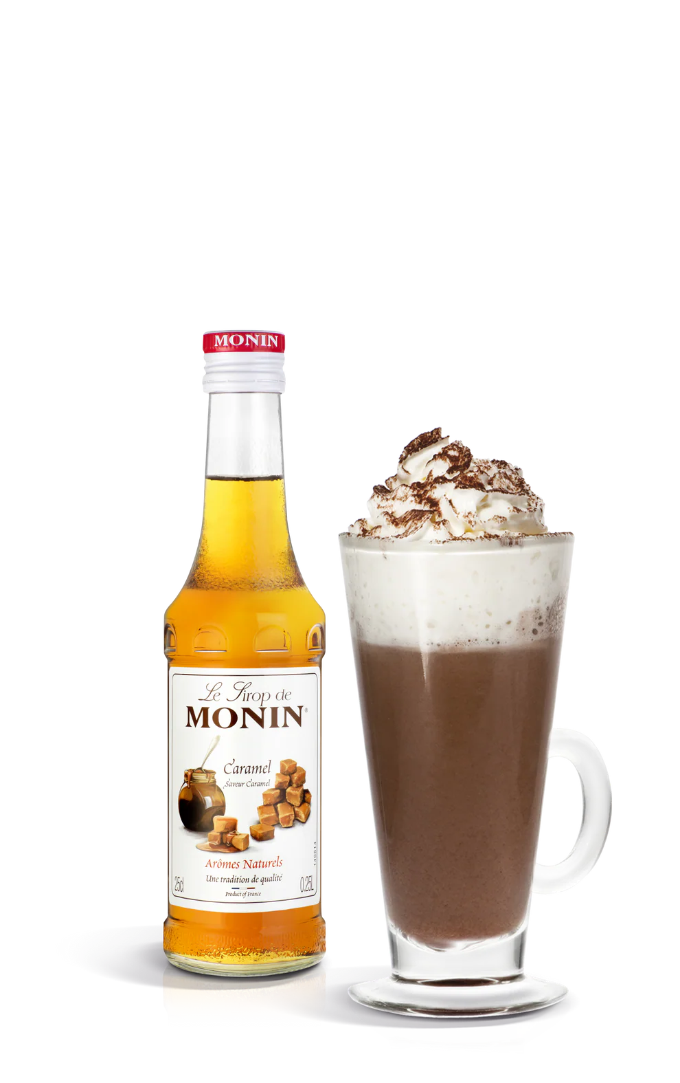 Monin caramel syrup bottle next to a glass of hot chocolate with whipped cream on a white background