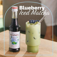 Blueberry_matcha_syrup_bottle_next_to_iced_matcha_latte_drink_in_glass_with_blueberries