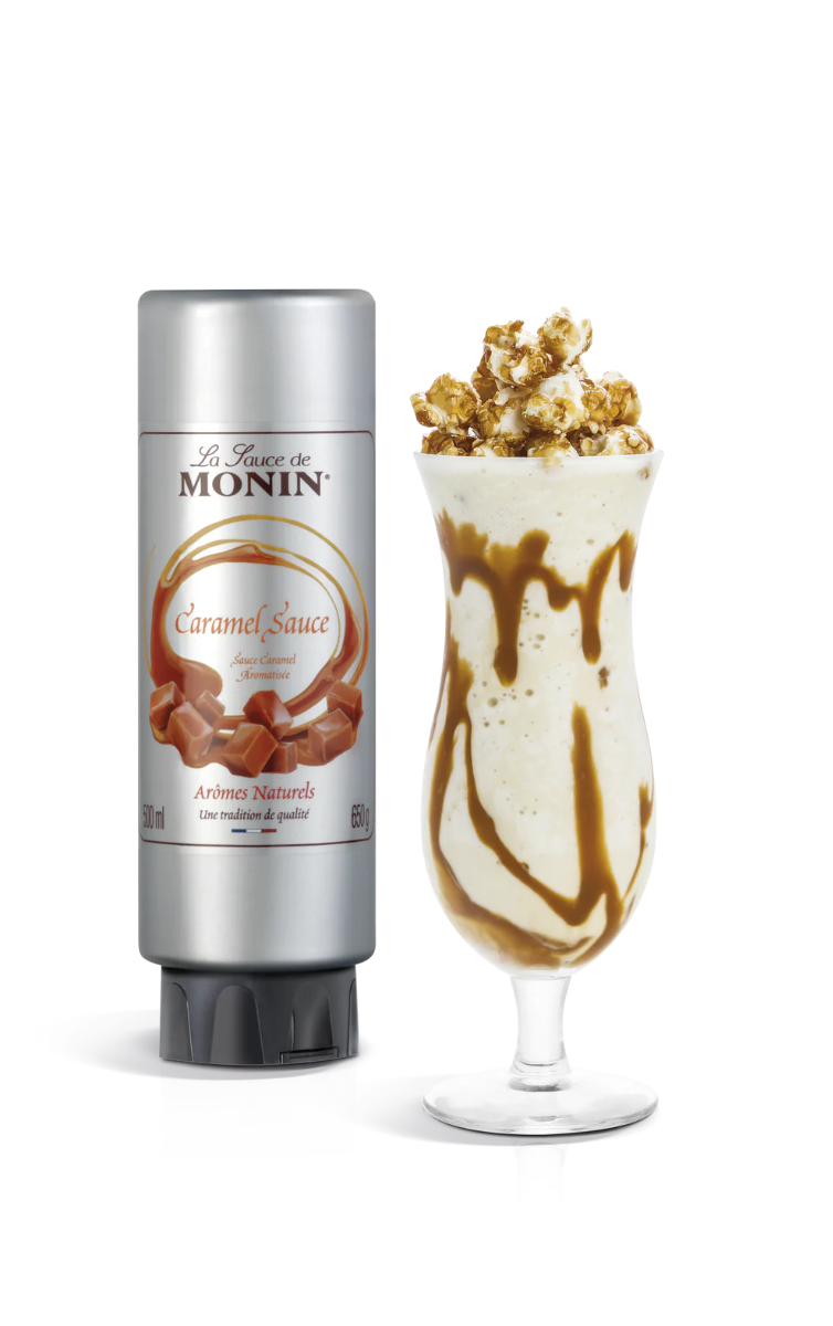 A 500ml bottle of Monin Caramel Sauce next to a glass of milkshake topped with caramel sauce.