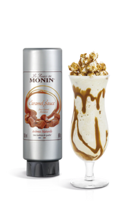 A 500ml bottle of Monin Caramel Sauce next to a glass of milkshake topped with caramel sauce.