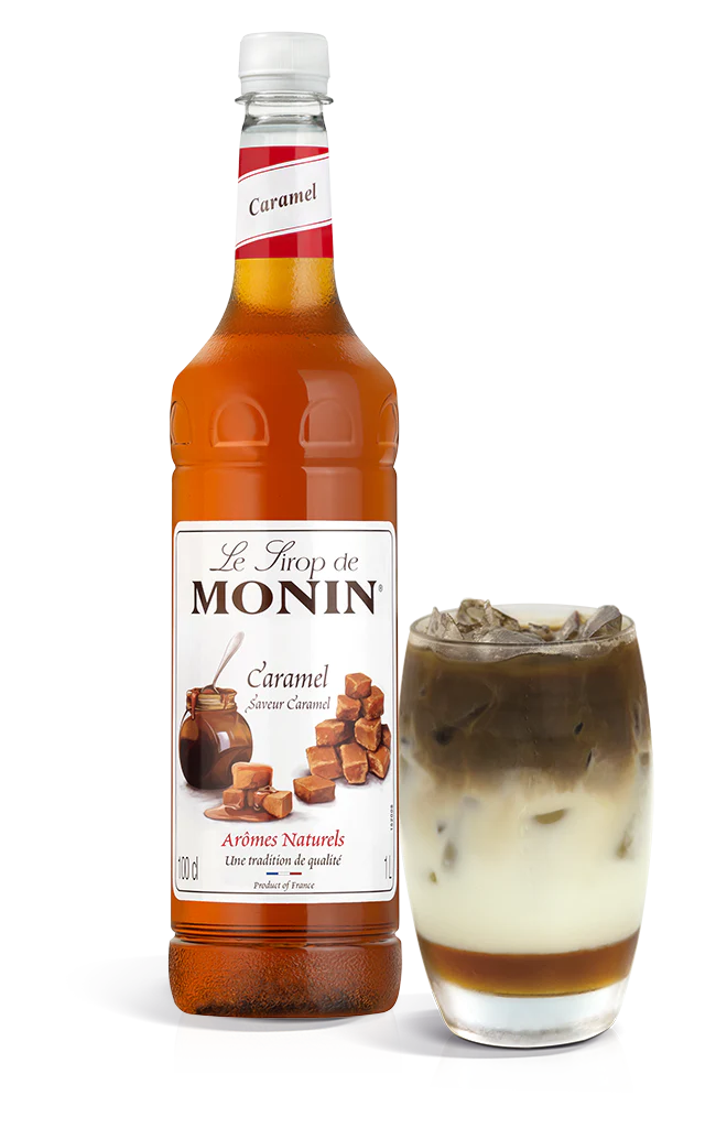 A bottle of Monin Caramel Syrup with a glass of caramel latte next to it.