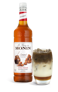 A bottle of Monin Caramel Syrup with a glass of caramel latte next to it.