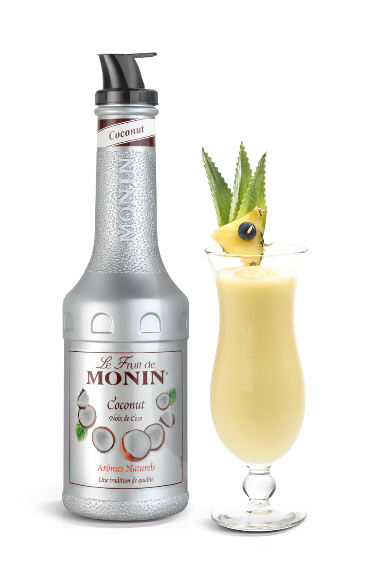 A bottle of Monin Coconut Puree with a decorative glass of coconut drink garnished with a pineapple slice and coconut on top.