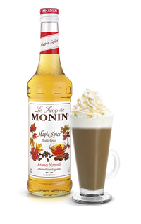 Monin Maple Spice syrup bottle with a glass of hot chocolate topped with whipped cream on a white background