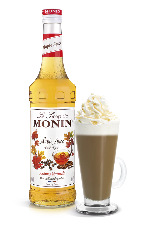 Monin Maple Spice syrup bottle with a glass of hot chocolate topped with whipped cream on a white background
