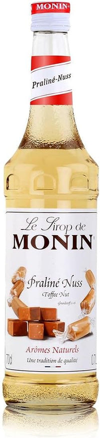 A bottle of Monin Praline Syrup with a label showing the brand name and praline nuts. The syrup is in a clear bottle and appears to be a golden color.