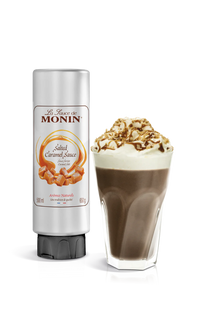 A bottle of Monin Salted Caramel Sauce next to a glass of dessert topped with caramel sauce and nuts.