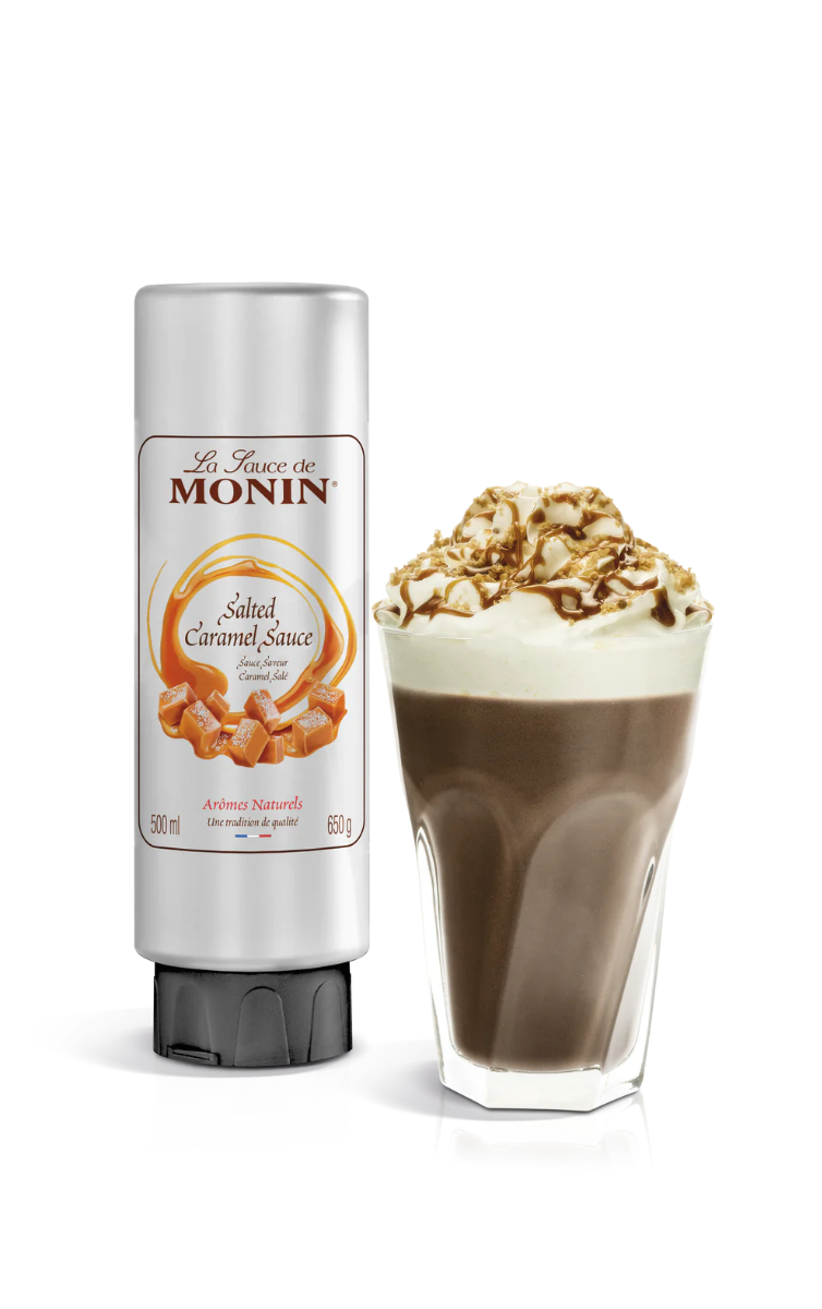 A bottle of Monin Salted Caramel Sauce next to a glass of dessert topped with caramel sauce and nuts.
