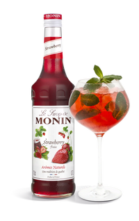 Monin strawberry syrup bottle with a glass of strawberry cocktail on a white background