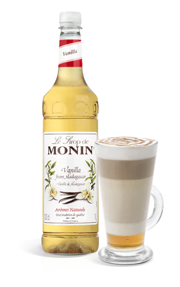 Monin vanilla syrup bottle with a glass of latte on a white background