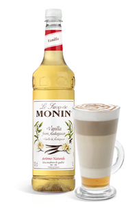 Monin vanilla syrup bottle with a glass of latte on a white background
