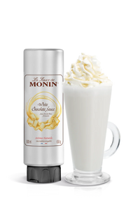 A bottle of Monin White Chocolate Sauce next to a glass of coffee topped with whipped cream.