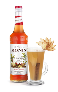 Monin Winter Spice syrup bottle with a glass of hot beverage garnished with apple slices on a white background