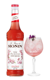 Monin Cherry Blossom syrup bottle beside pink cocktail in stemmed glass with edible flower garnish, cocktail recipe inspiration image