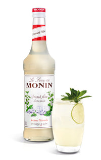 Monin syrup bottle with a glass of a drink garnished with mint and a slice of lime on a white background