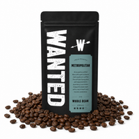 A black stand-up coffee bag labeled WANTED Metropolitan Whole Bean, surrounded by scattered roasted coffee beans on a white background.