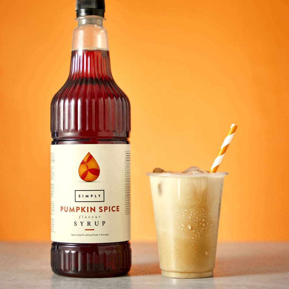 A bottle of Simply Pumpkin Spice Flavored Syrup stands next to a clear plastic cup filled with iced coffee and a striped paper straw, set against a solid orange background.