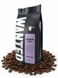 A black coffee bag labeled 'WANTED' with a lavender panel reading 'Colombian Decaf' and 'Whole Bean,' surrounded by scattered coffee beans on a white background.