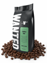A black coffee bag labeled 'WANTED Temple Bar' stands upright on a white background, surrounded by scattered roasted coffee beans. The bag has a mint green label and large distressed white lettering.