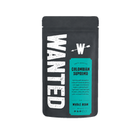 A matte black coffee bag with a large distressed white 'WANTED' logo on the left and a teal label reading 'COLOMBIAN SUPREMO' and 'WHOLE BEAN' on the front, shown on a plain white background.