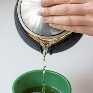 Black neoprene insulated tea cozy covering glass teapot with stainless lid