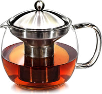 Hands placing loose leaf tea into stainless steel infuser over glass teapot
