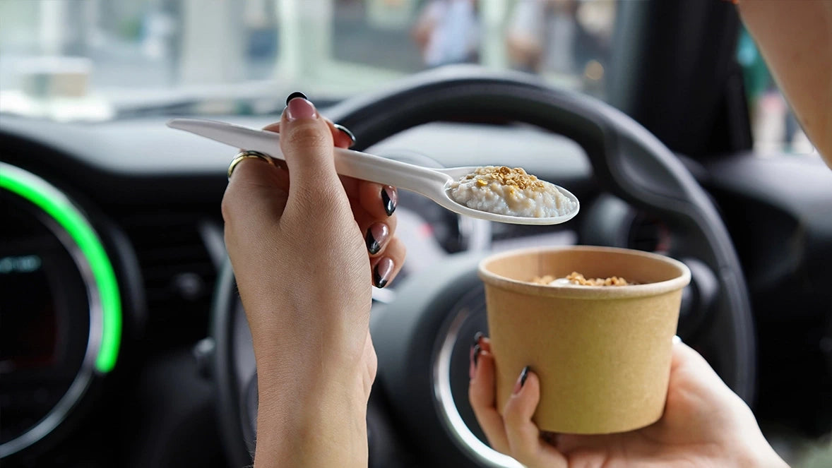 Lifestyle stock photo of hands using Go-Pak premium paper cutlery spoon with food above paper cup inside car.