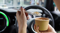 Lifestyle stock photo of hands using Go-Pak premium paper cutlery spoon with food above paper cup inside car.