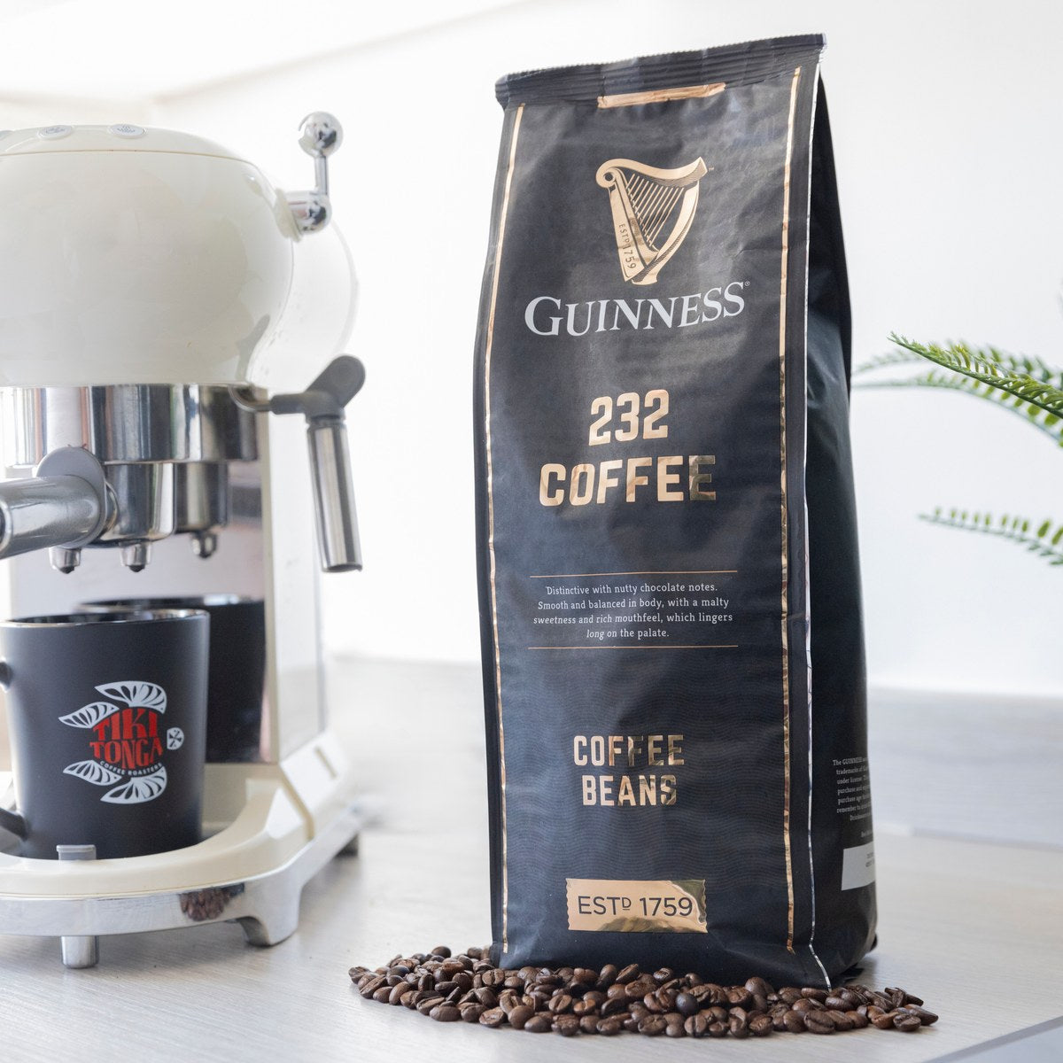 Guinness 232 Coffee Beans 1kg bag beside an espresso machine and grinder with coffee beans