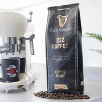 Guinness 232 Coffee Beans 1kg bag beside an espresso machine and grinder with coffee beans