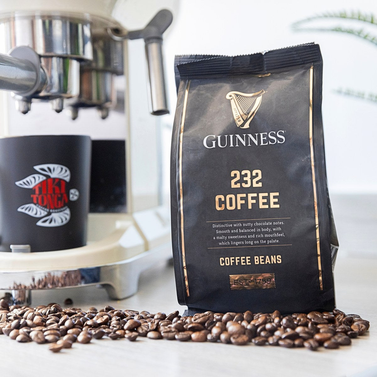 Guinness 232 Coffee Beans 227g bag beside an espresso machine with scattered coffee beans
