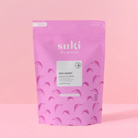 Pink Suki tea pouch packaging with red berry loose leaf pyramids on light pink background
