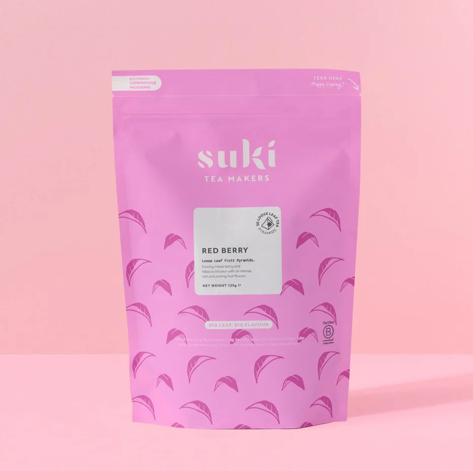 Pink Suki tea pouch packaging with red berry loose leaf pyramids on light pink background