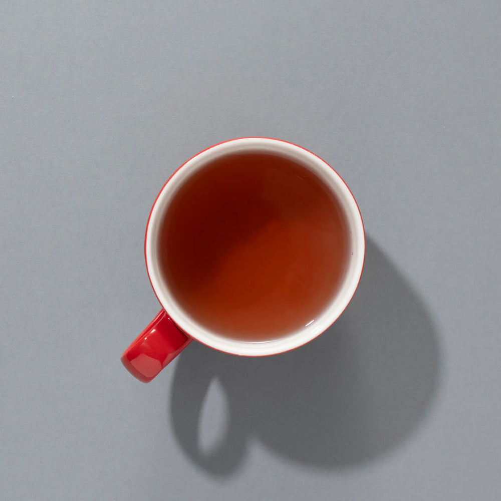 Red mug filled with vibrant hibiscus berry tea on grey background