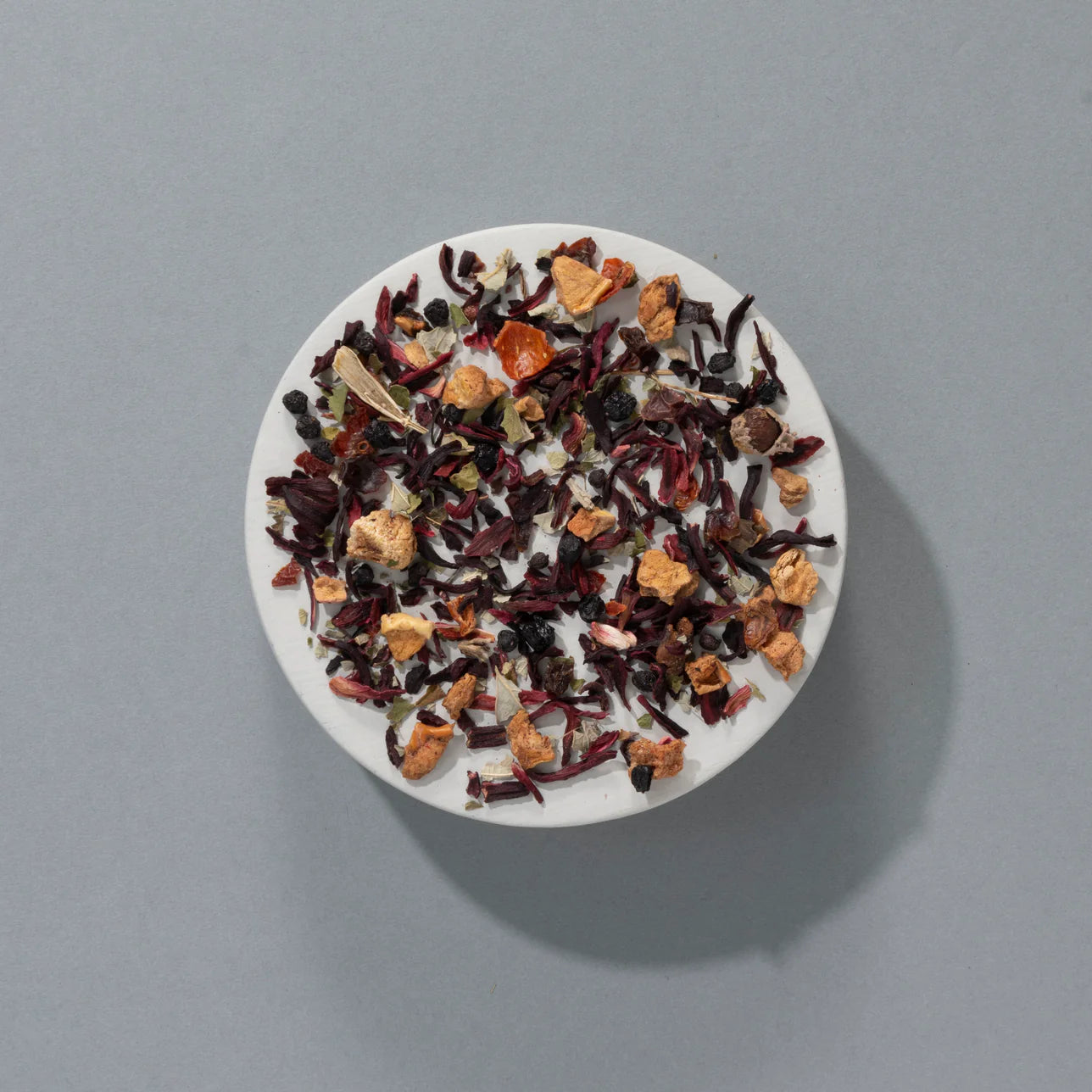 White bowl of mixed hibiscus loose leaf tea with dried berries and flowers on grey background